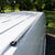 Silver LoadSpan roof rail with L-track channel and end cap mounted on the roof of a white Mercedes Sprinter parked outdoors