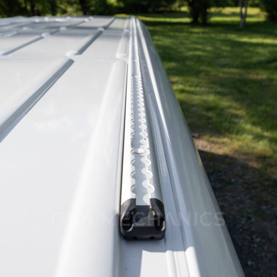 LoadSpan roof rail with scalloped L-track and black end cap mounted along a white Mercedes Sprinter roof edge